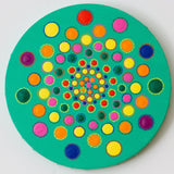 Colourful dot mandalaa on round canvas, red yellow pink green blue purple on green background