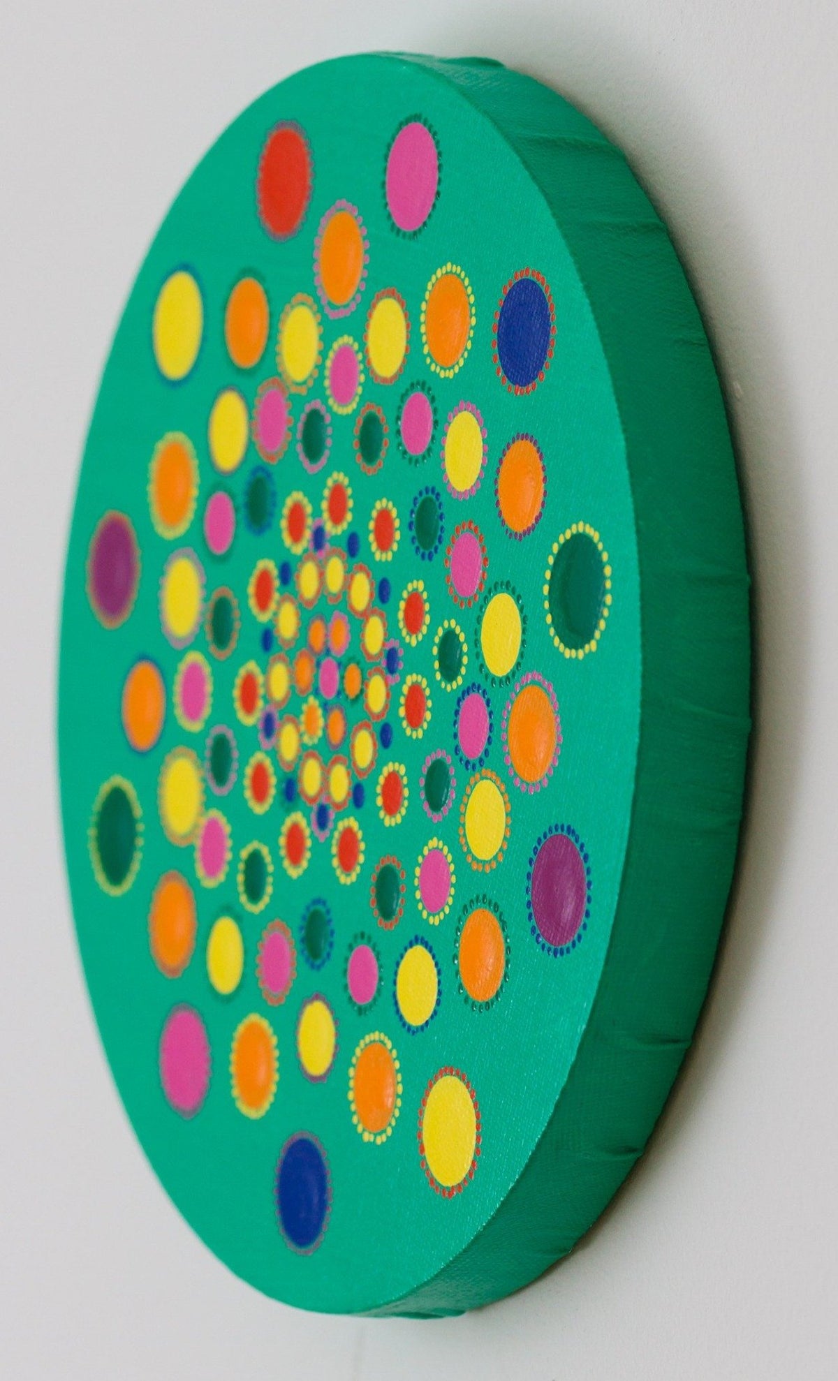Colourful dot mandala on round canvas, yellow green blue pink orange purple on green background