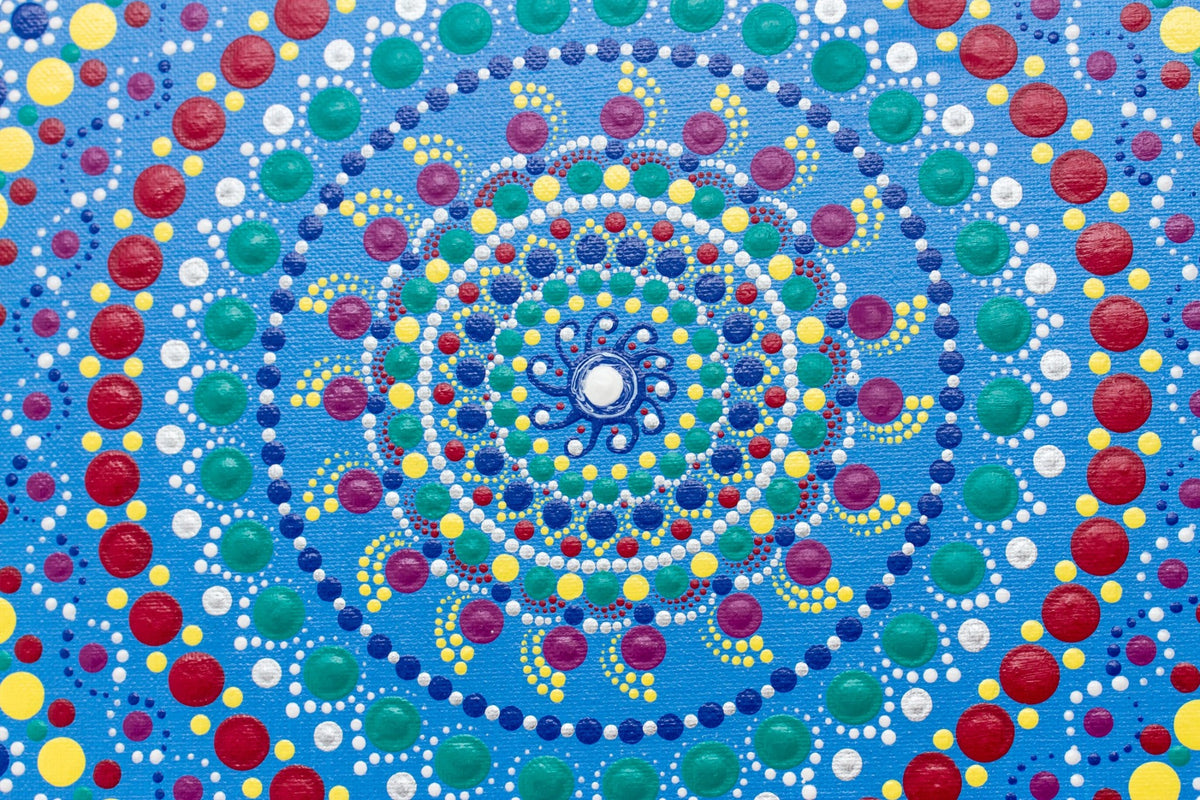 Colourful dot mandala detail, red yellow green purple white on blue background